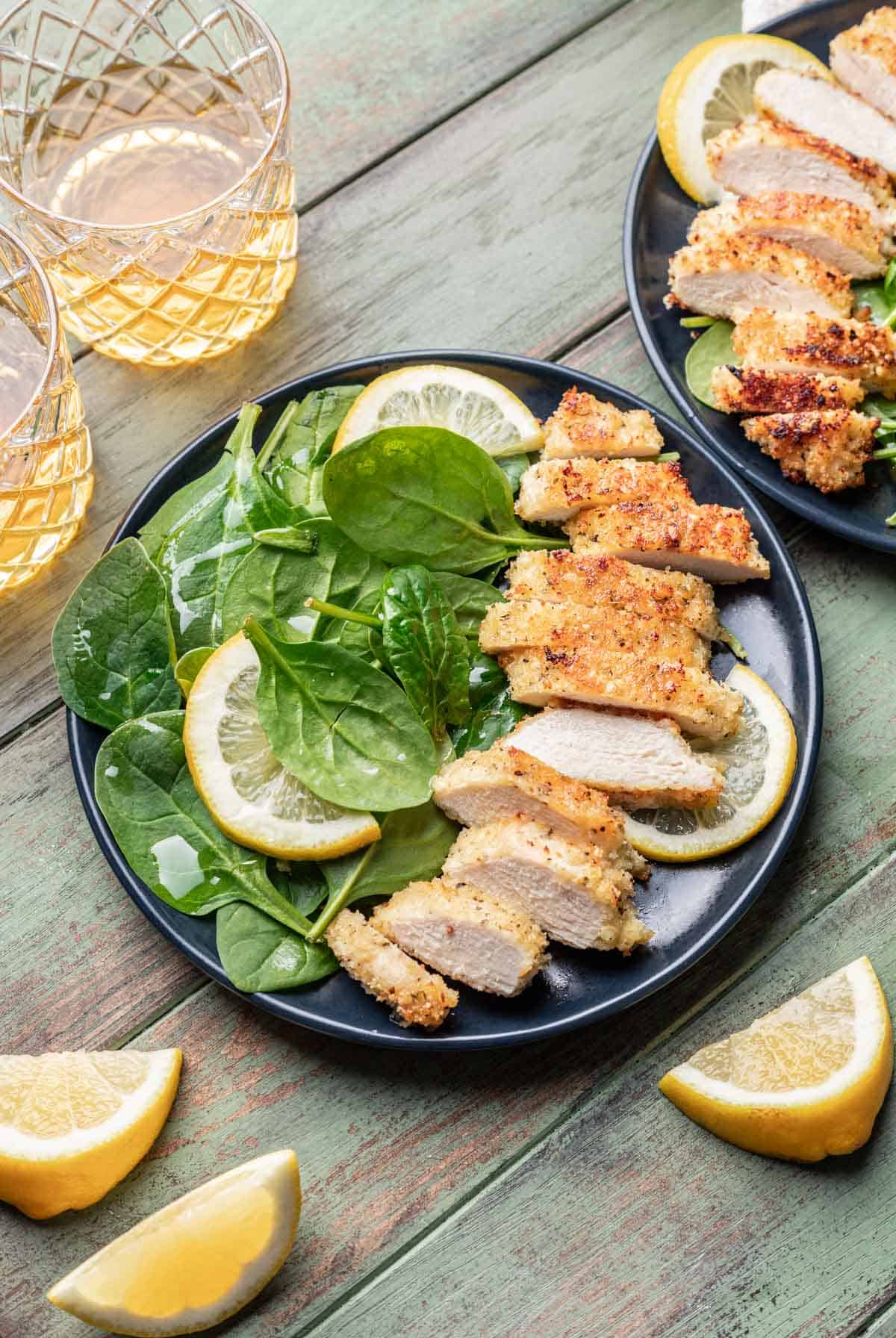 Panko chicken on a plate with a spinach salad and lemon wedges.