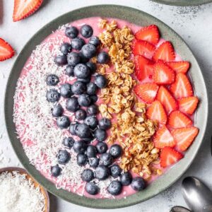 Strawberry smoothie bowl topped with coconut, blueberries, granola, and strawberries.