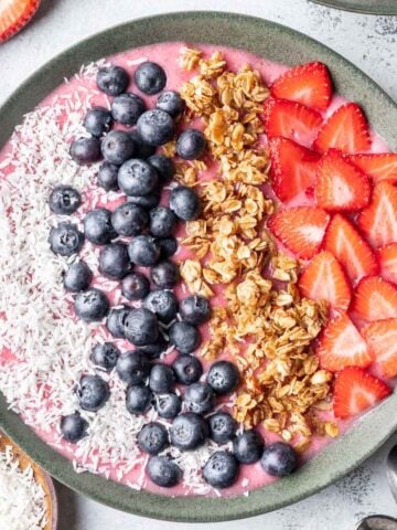 Strawberry smoothie bowl topped with coconut, blueberries, granola, and strawberries.