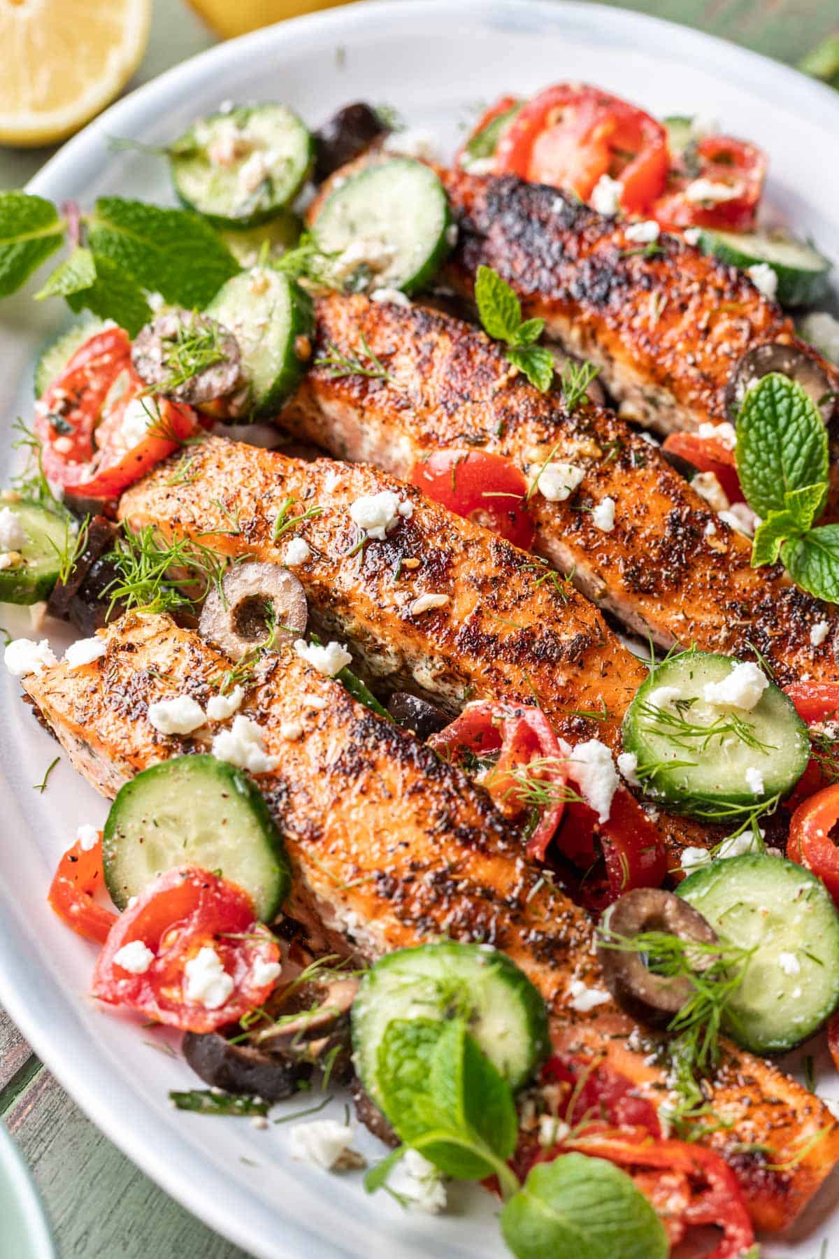 Greek salmon on a serving platter with cucumbers, olives, and tomatoes.