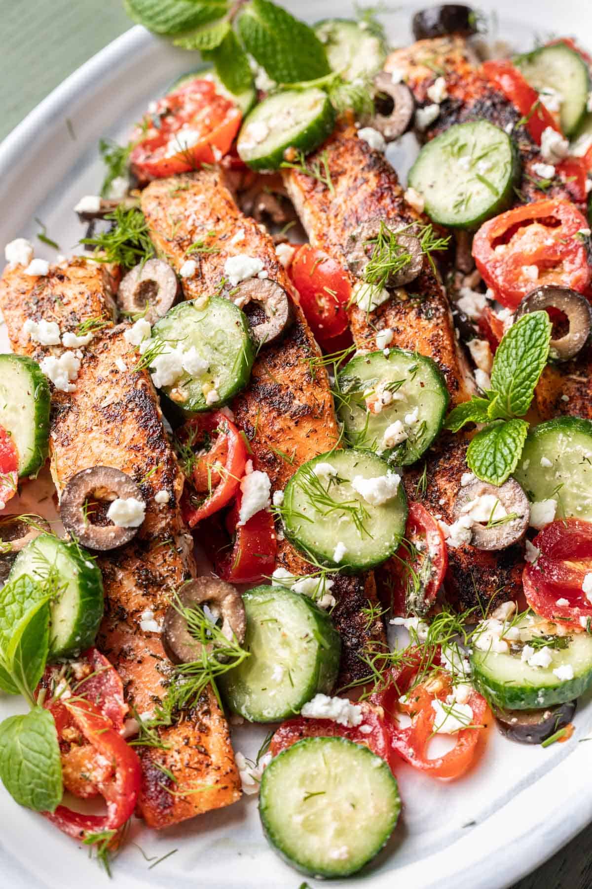 Greek salmon on a serving platter with cucumber, dill, mint, and tomatoes.