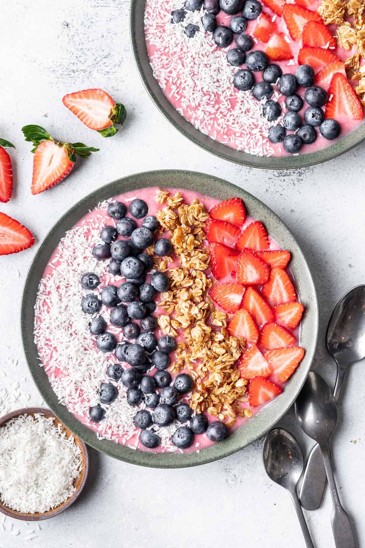 Strawberry smoothie bowl in a green bowl on a white backdrop.