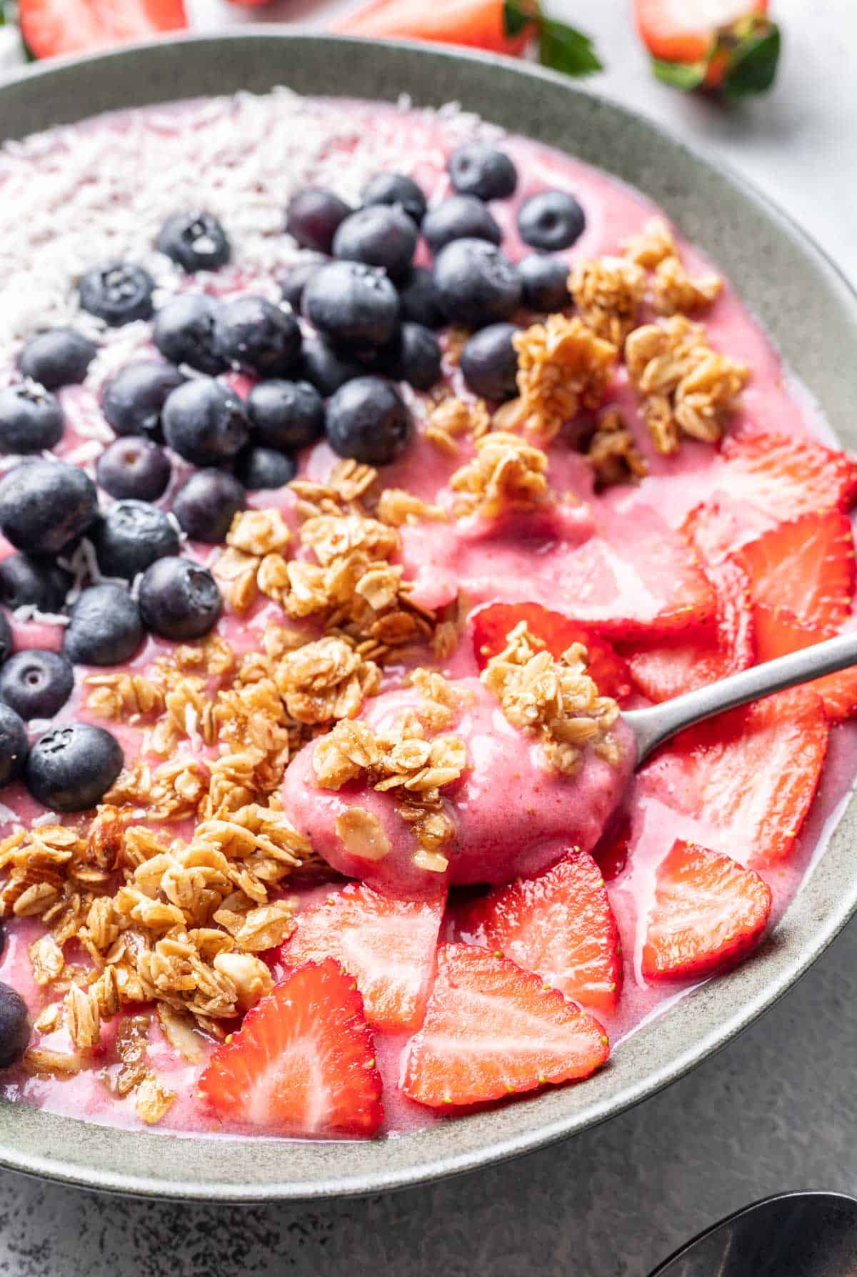 Strawberry smoothie bowl with a spoon scooping some out.