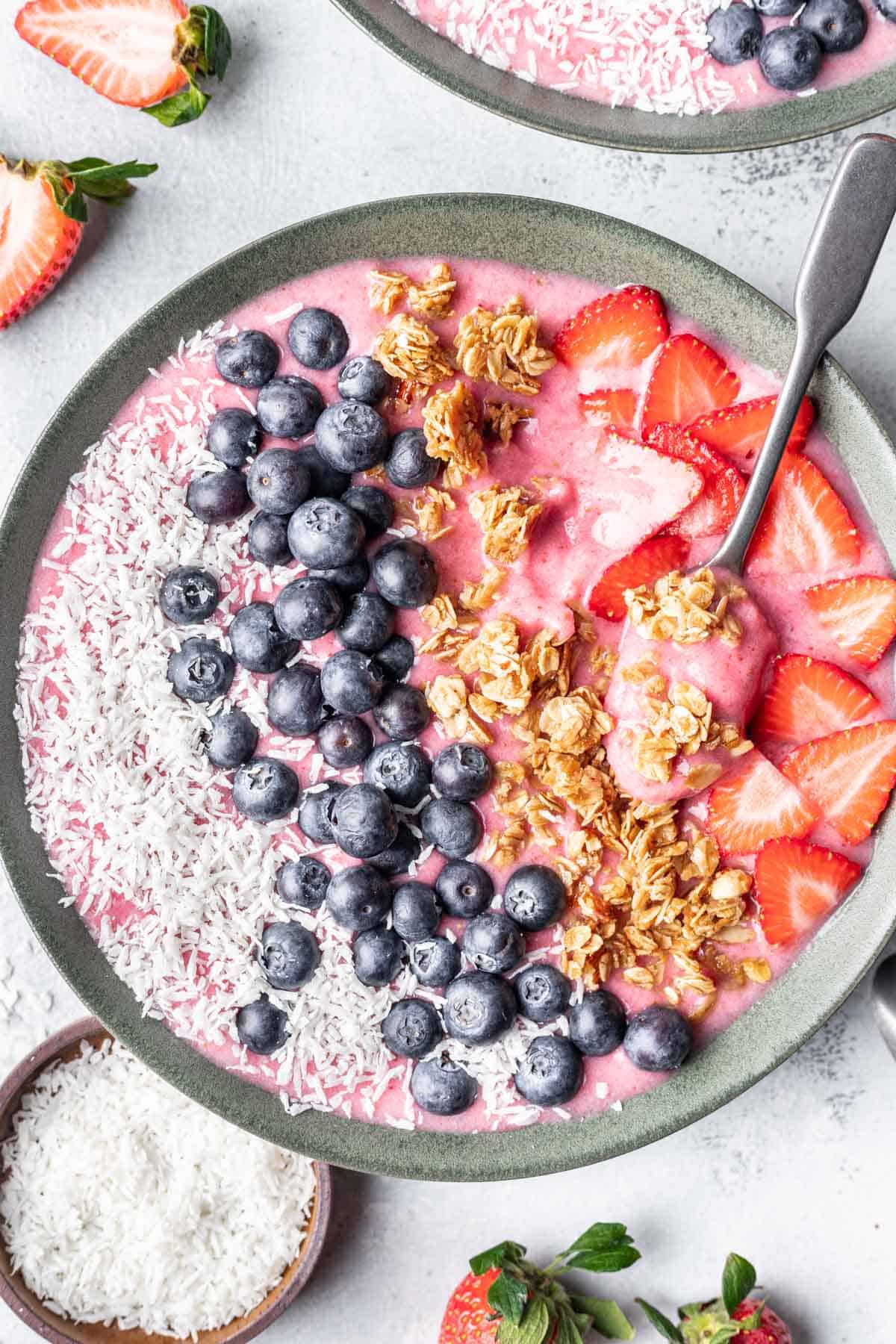 Strawberry smoothie bowl topped with coconut, blueberries, granola, and strawberries.