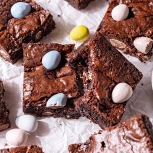 Mini egg brownies on parchment paper with easter eggs around it.