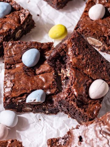 Mini egg brownies on parchment paper with easter eggs around it.