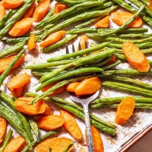 Roasted green beans and carrots on a baking sheet with a serving fork.