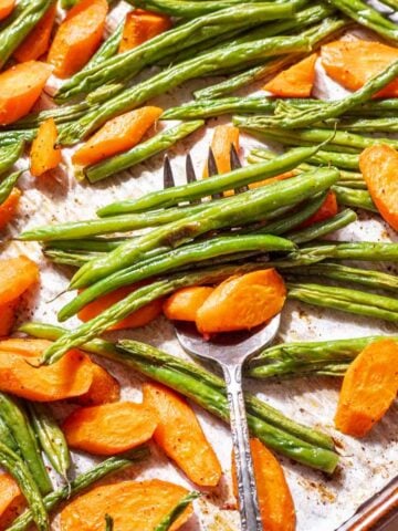 Roasted green beans and carrots on a baking sheet with a serving fork.