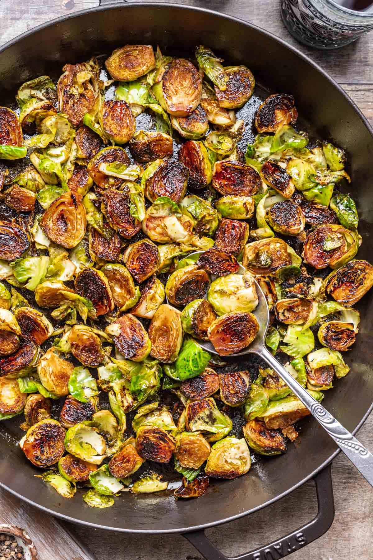 Maple balsamic brussels sprouts in a large skillet with a serving spoon.