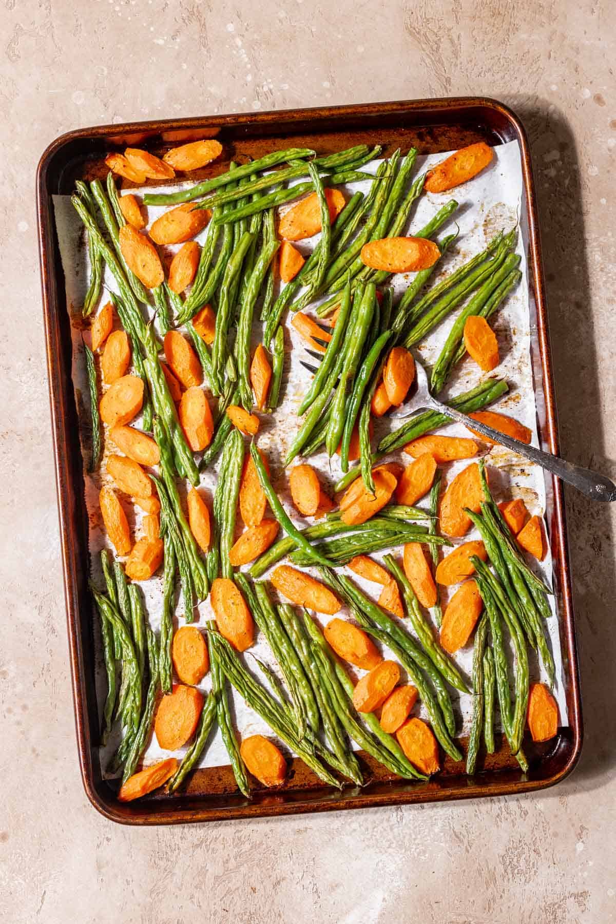Roasted green beans and carrots on a baking sheet after roasting.