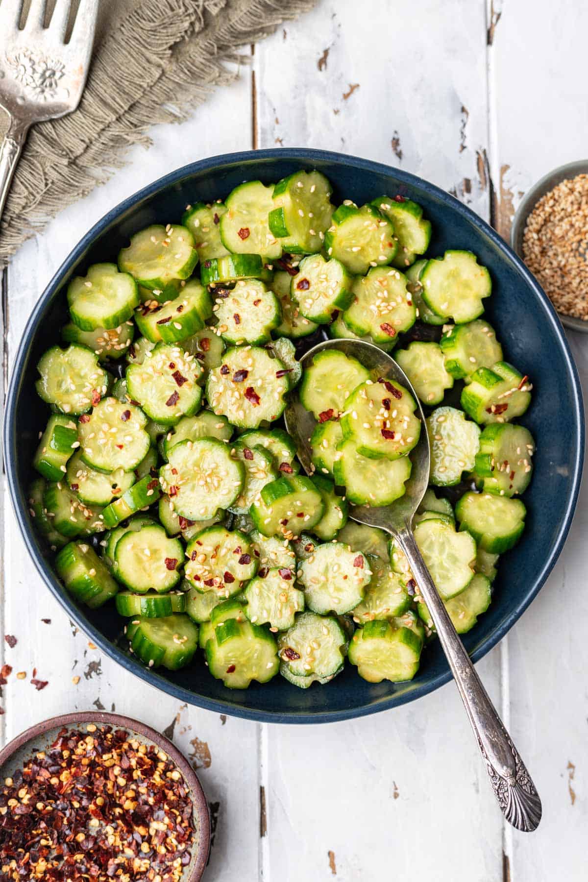 Spicy cucumber salad in a blue serving bowl with a spoon.