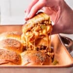 Cheesy sloppy joe slider held above a baking dish to show cheesiness.