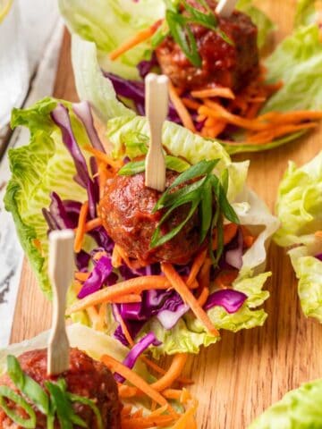 Spicy meatballs on a lettuce cup with shredded carrots and purple cabbage.