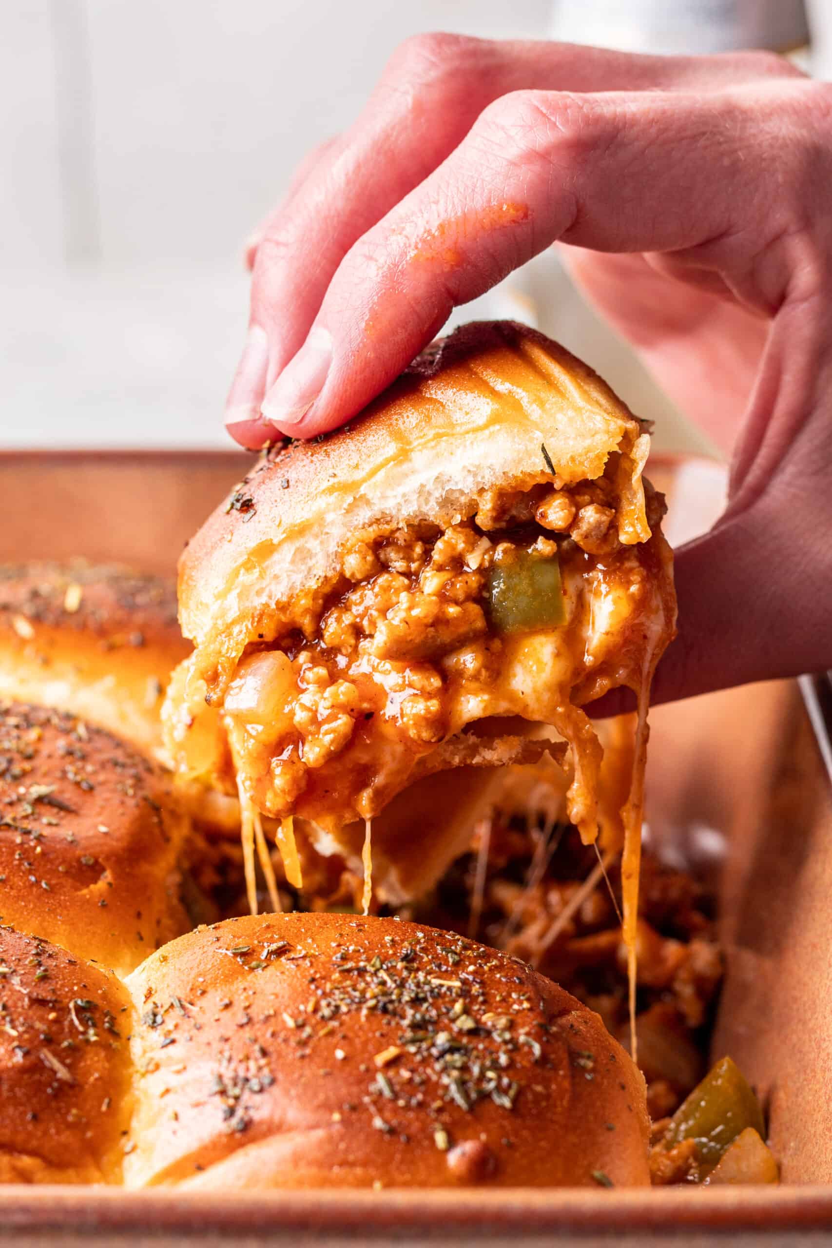 Cheesy sloppy joe slider being pulled out of the baking dish by a hand.