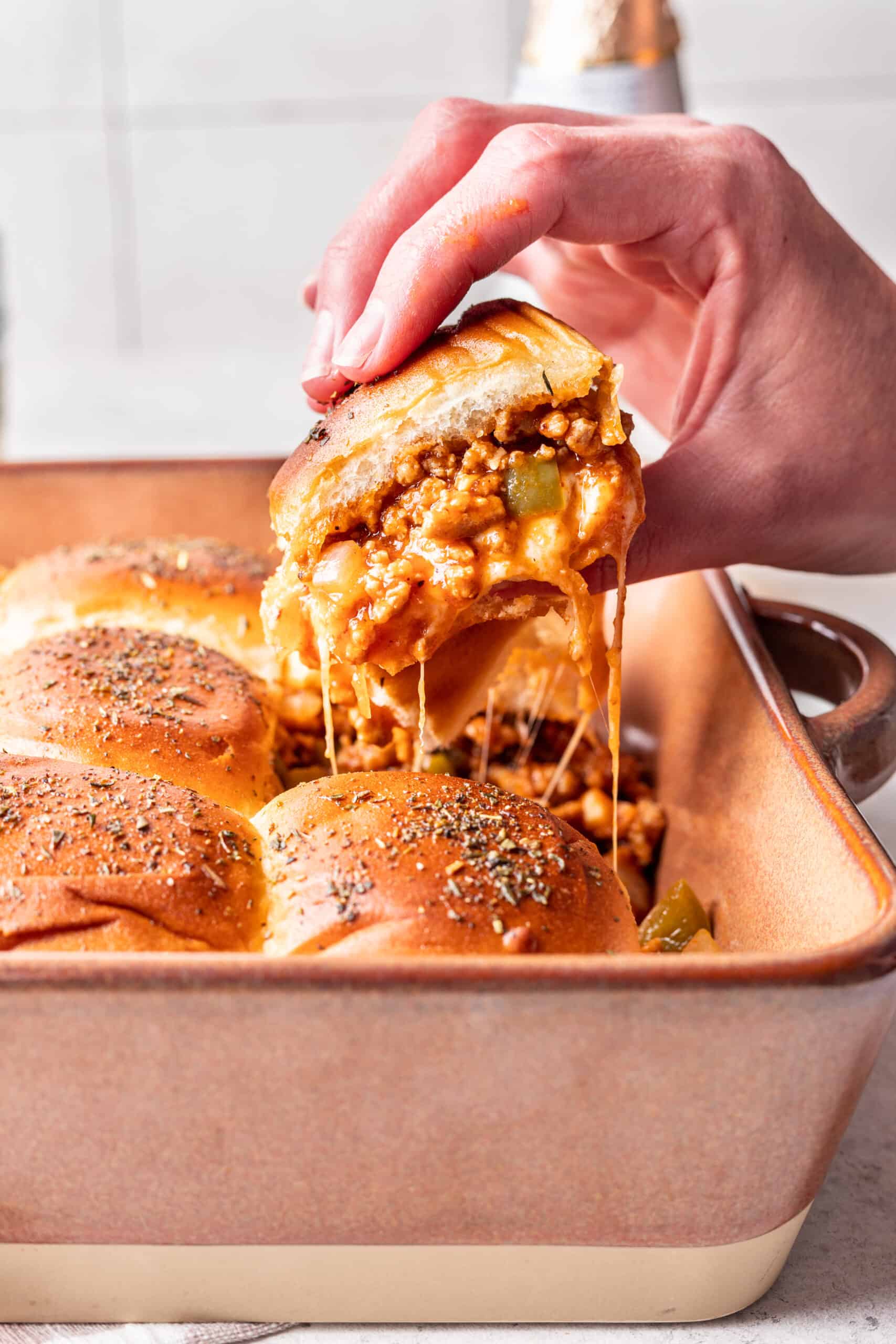 Cheesy sloppy joe slider held above a baking dish to show the cheesiness.