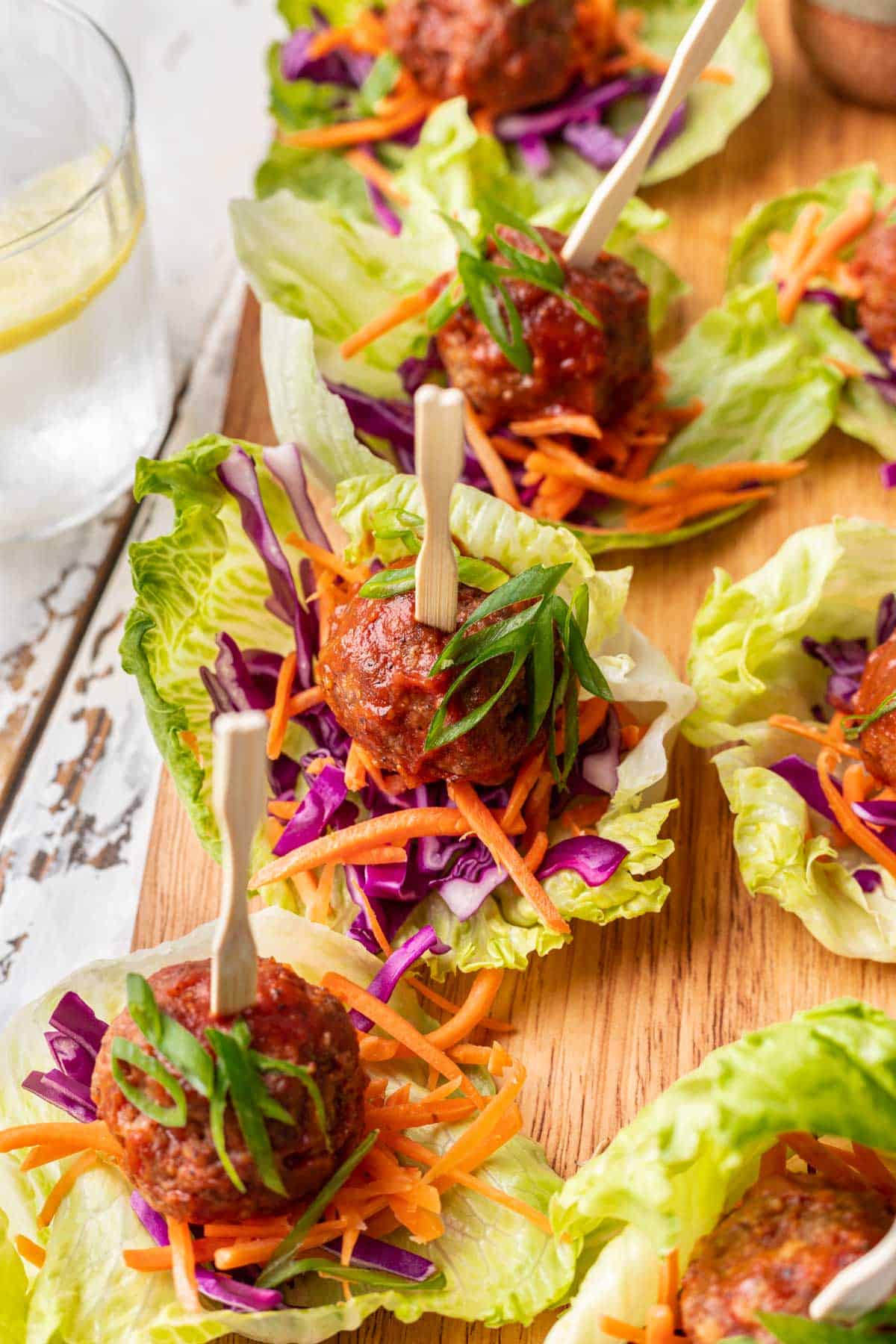 Spicy meatballs assembled on lettuce cups with shredded carrots and purple cabbage.