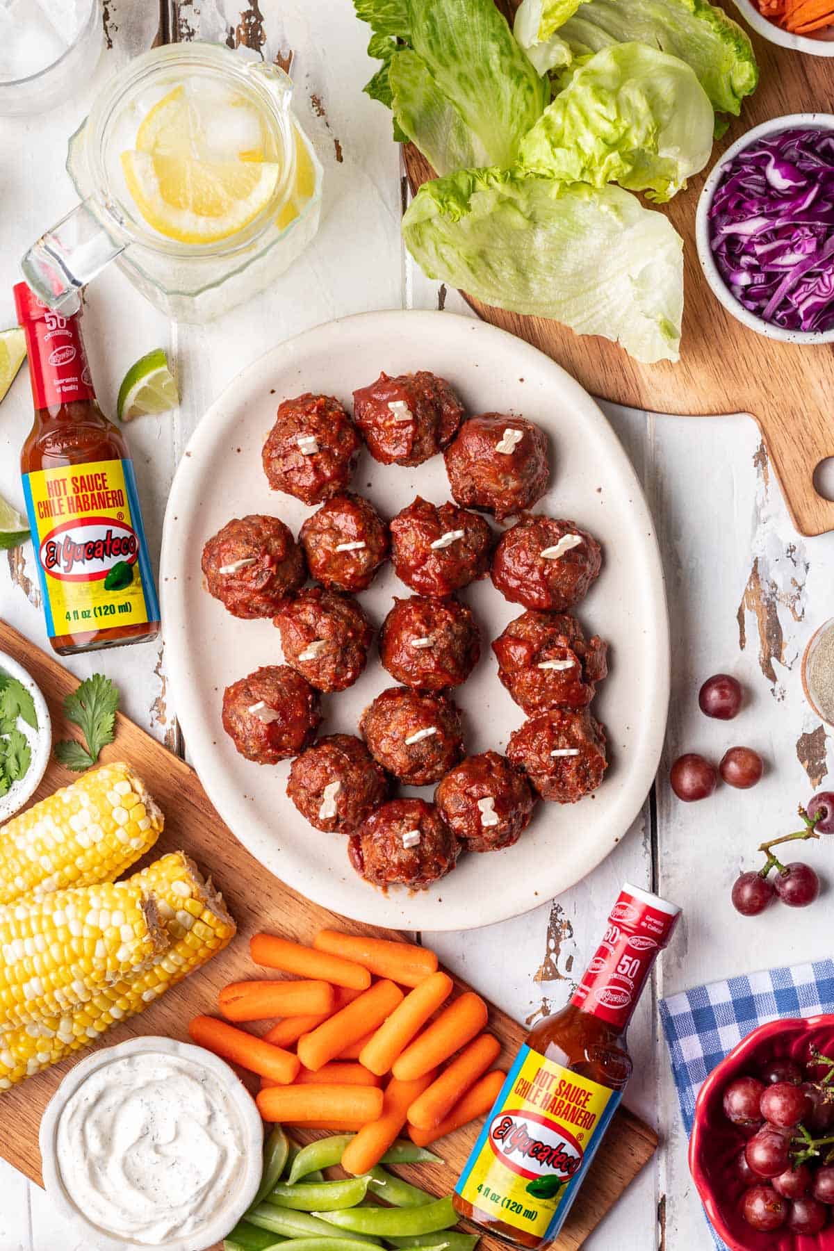 Spicy meatballs on a platter surrounded by other summer cookout foods.