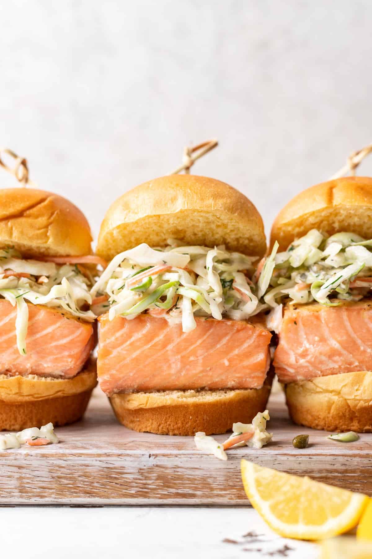 Salmon sliders with brioche buns and caper dill slaw on a serving tray.