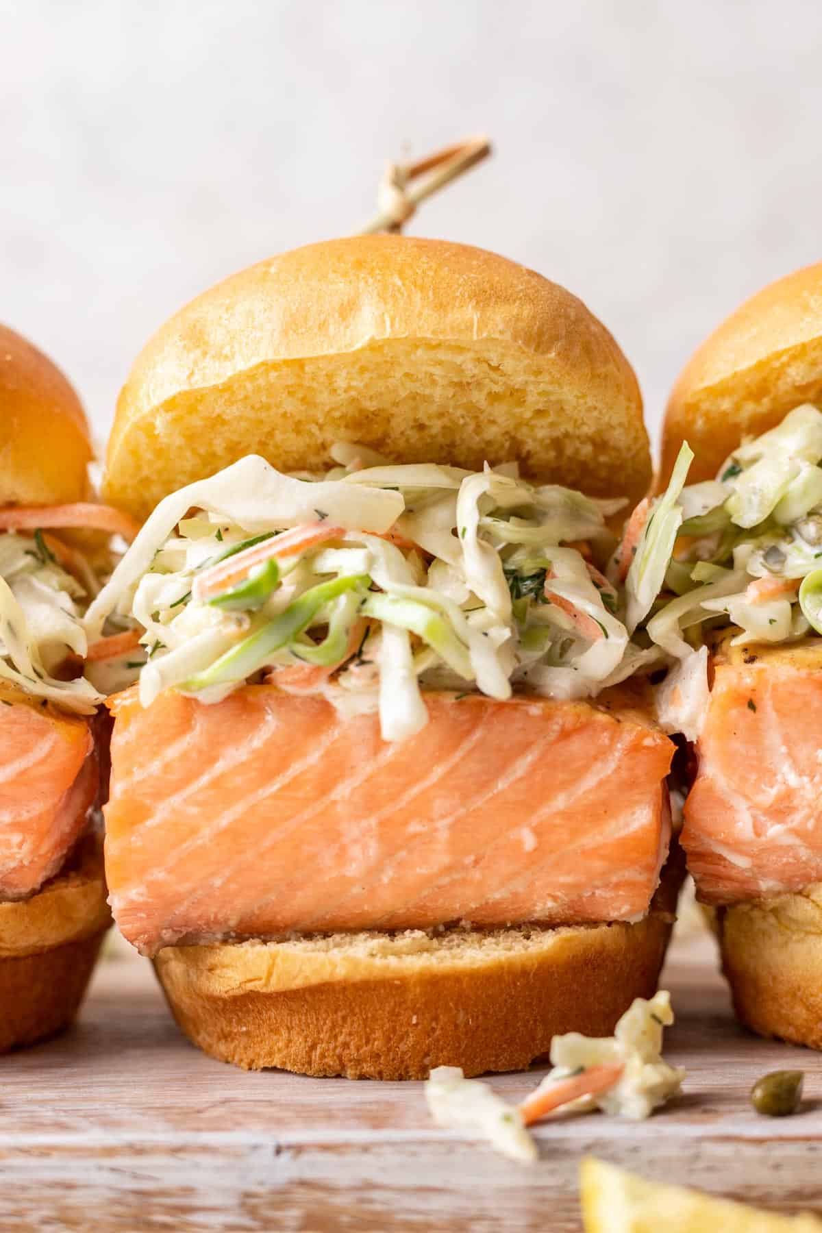 A closeup of a salmon slider on a brioche slider bun topped with coleslaw.