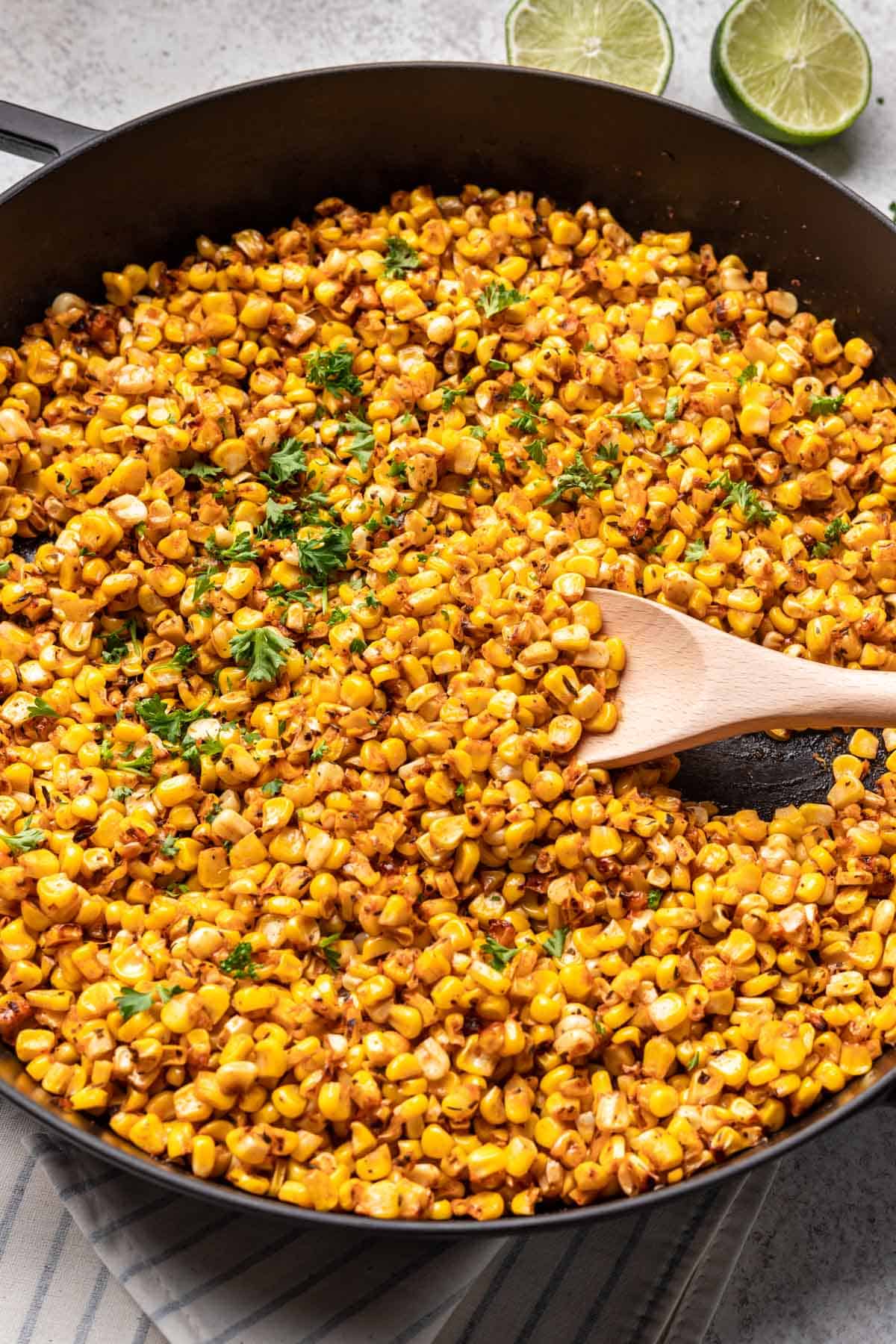 Blackened corn in a skillet with a wooden spoon.