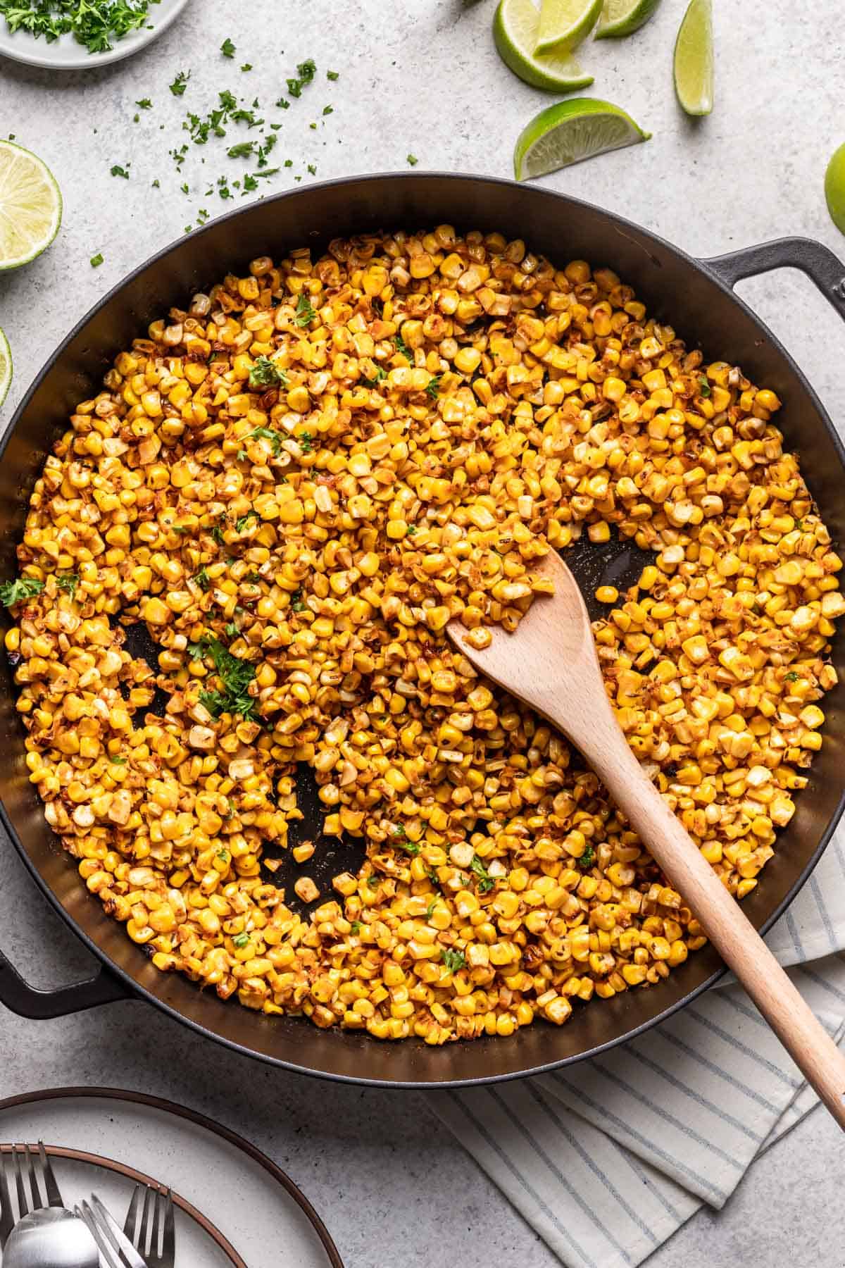 Blackened corn in a skillet with fresh limes and parsley.