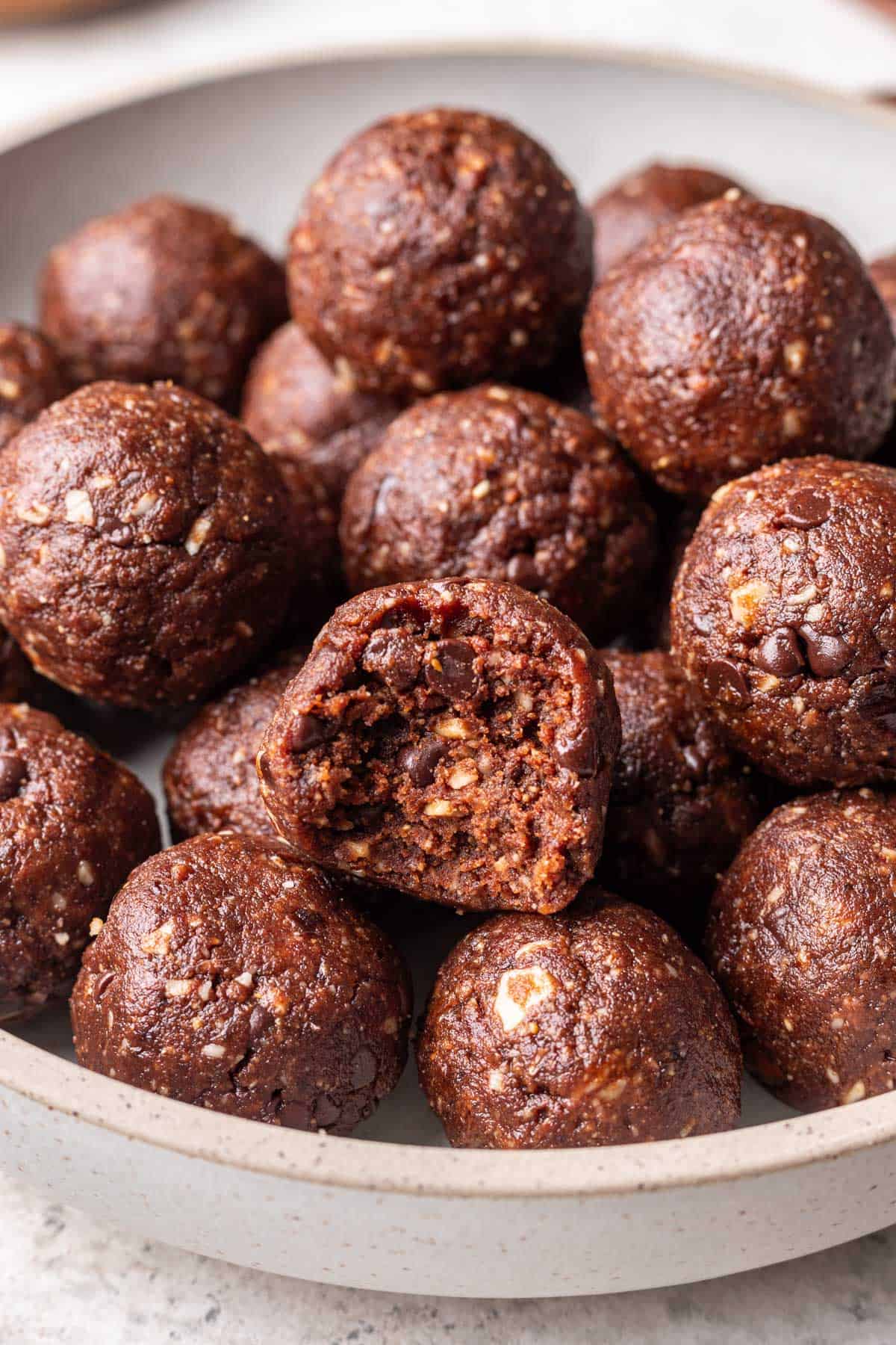 Chocolate bliss balls in a serving bowl, one has a bite taken out.