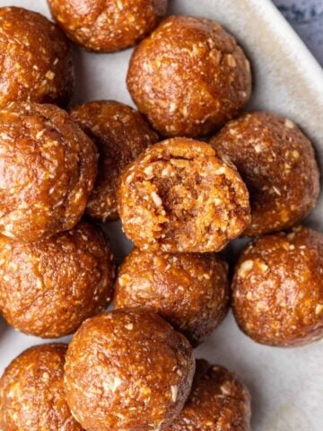 Apricot bliss balls on a serving platter with one with a bite taken out.