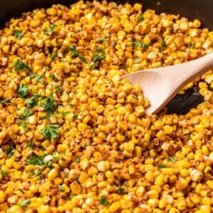 A wooden spoon scooping blackened corn out of a skillet.