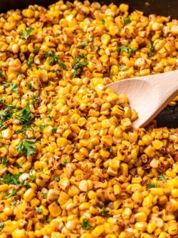 A wooden spoon scooping blackened corn out of a skillet.