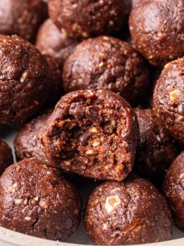 Chocolate bliss balls on a platter with one with a bite taken out.