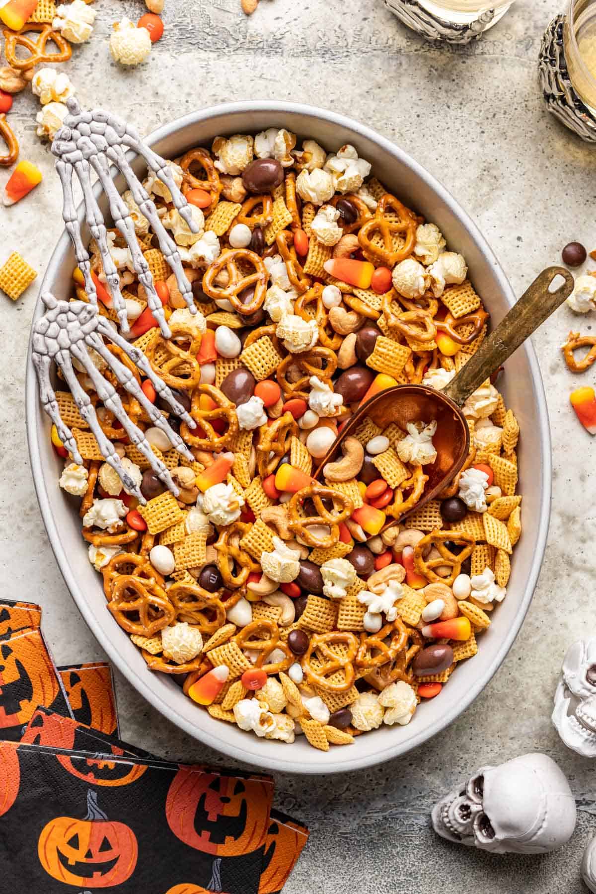 Halloween trail mix in a large serving bowl with fake skeleton hands and a metal scoop.