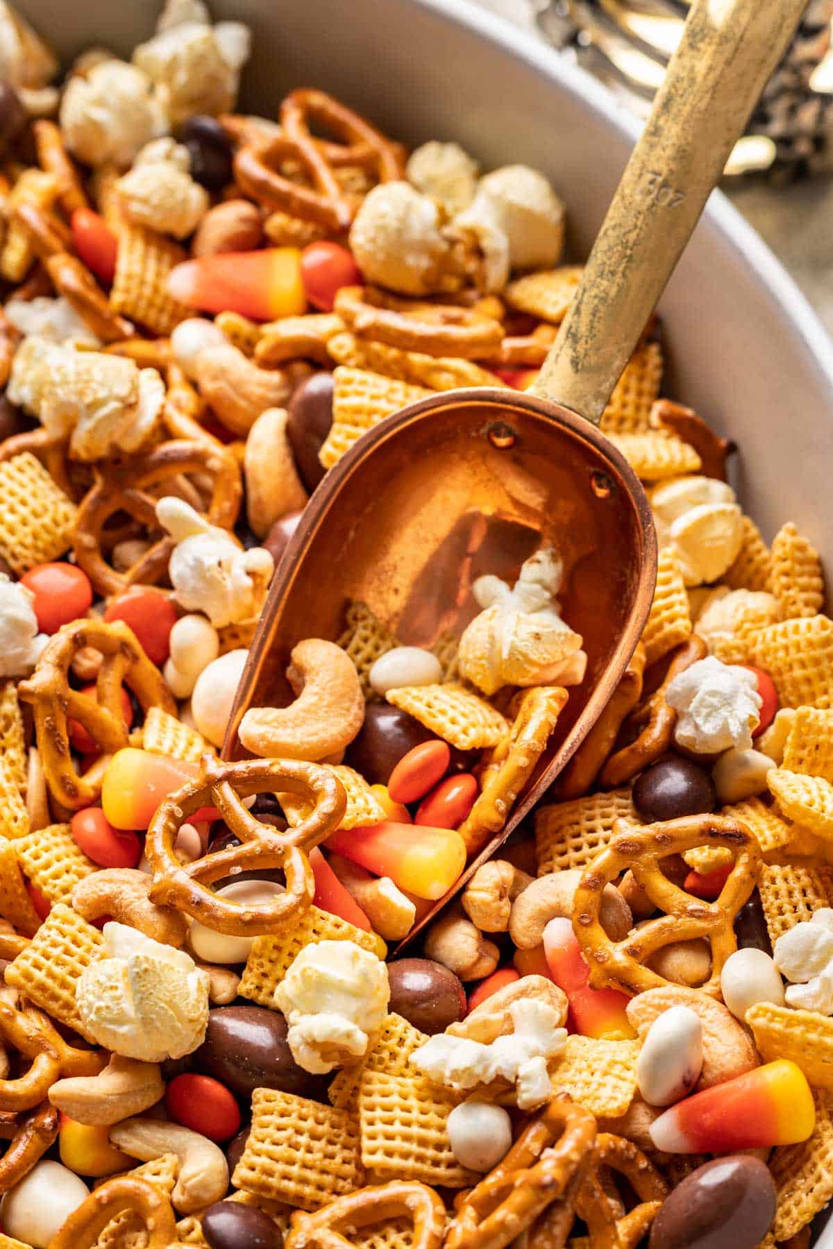 A metal scoop scooping halloween trail mix from a serving bowl.