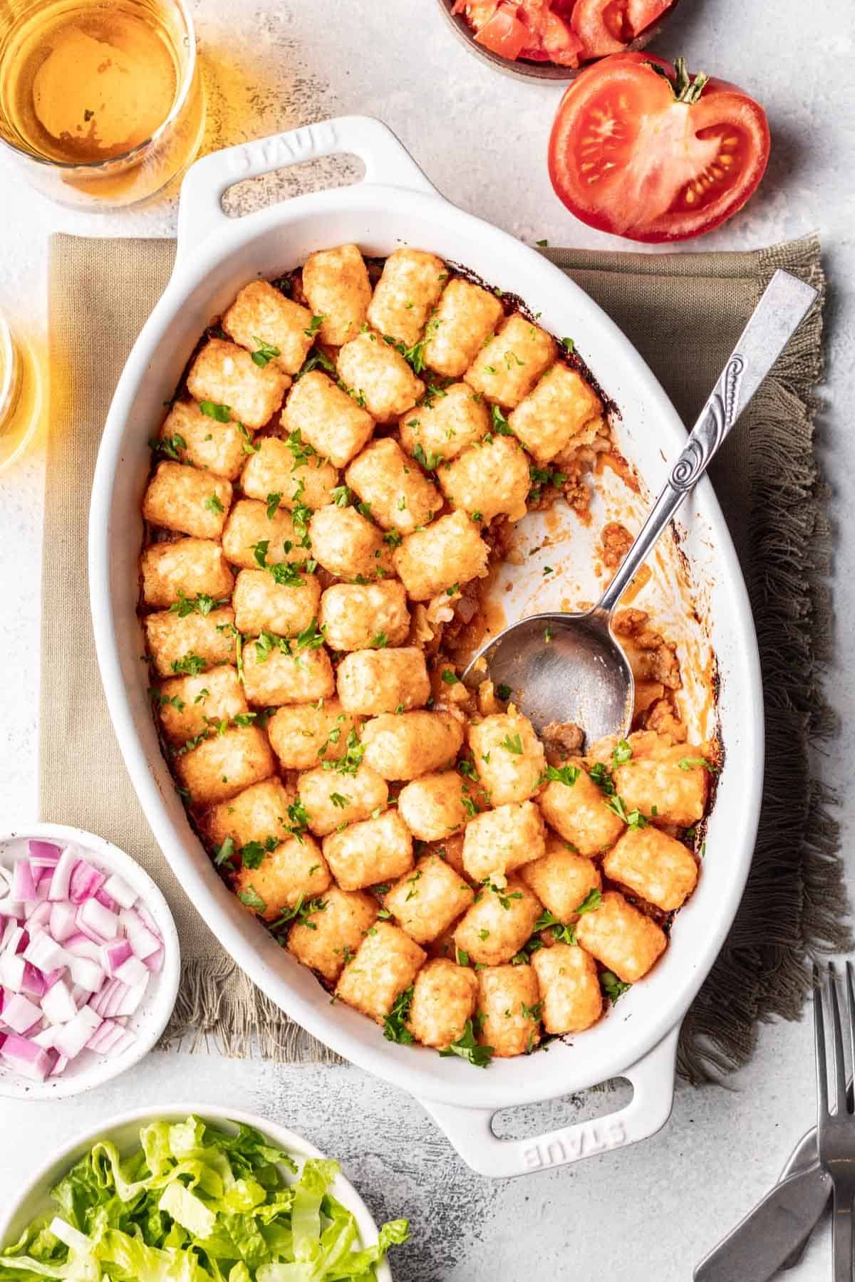 Cheeseburger tater tot casserole in an oval baking dish with a serving spoon.