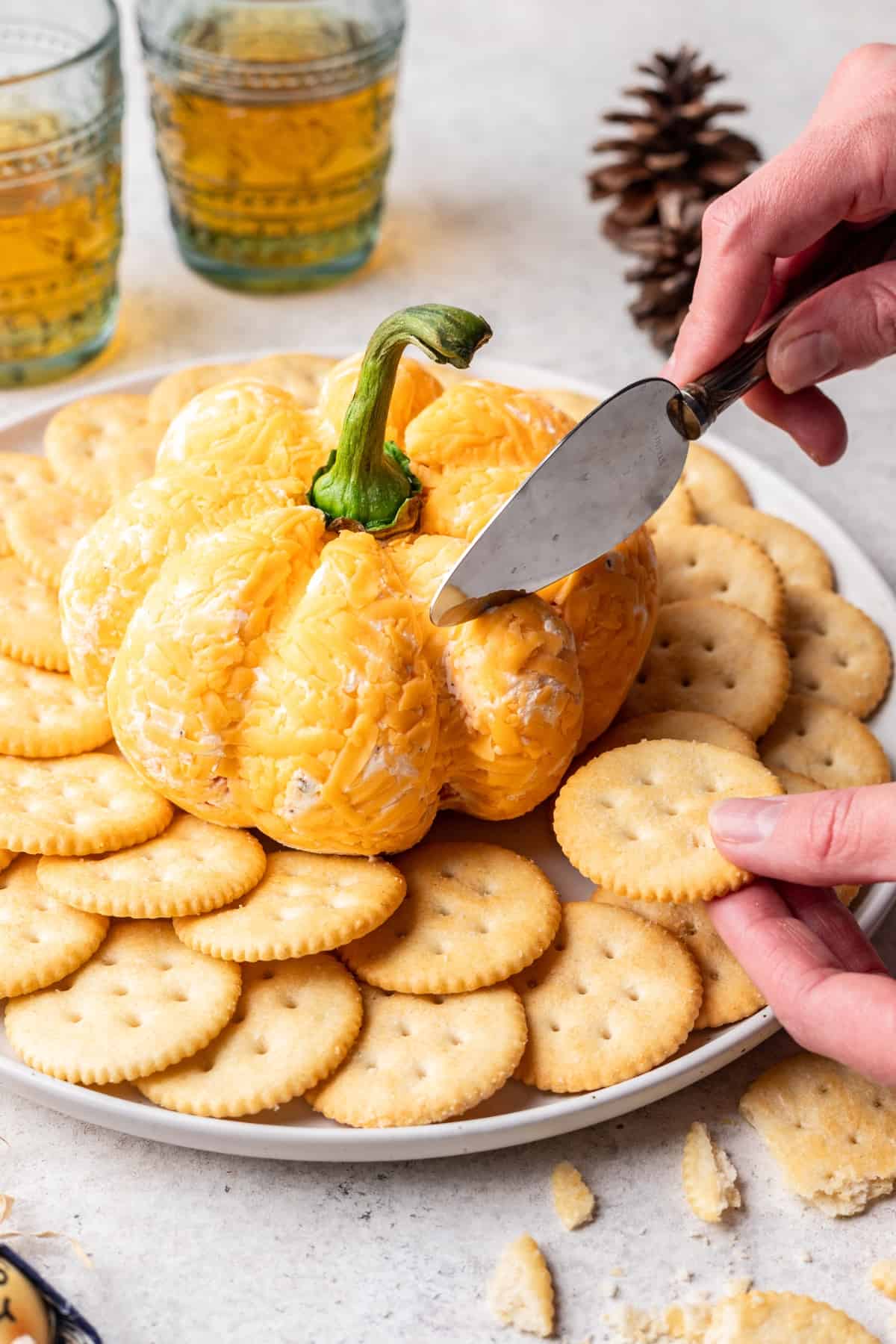 Pumpkin shaped cheese ball on a serving platter with a cheese knife cutting into it.