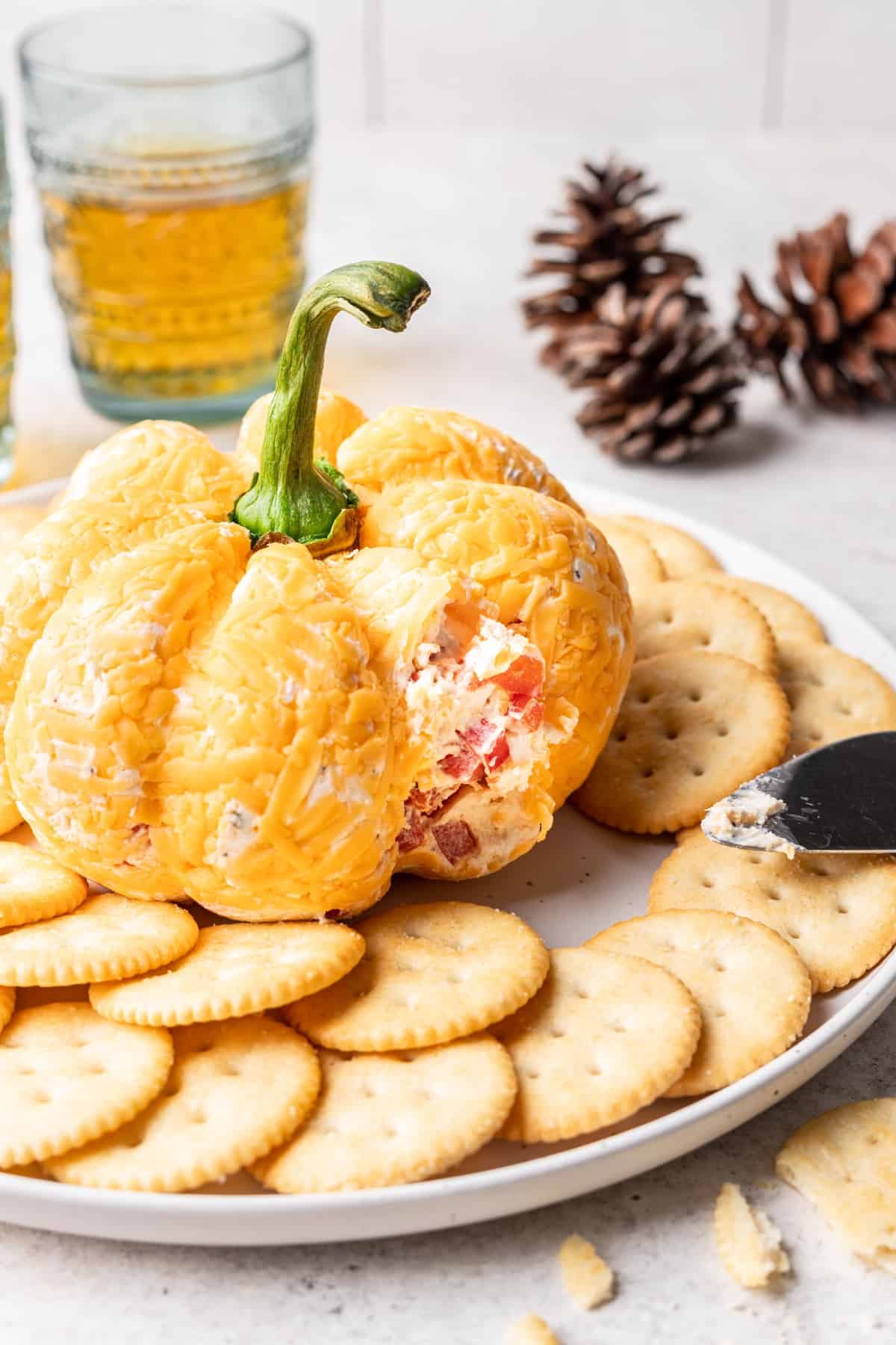 A pumpkin cheese ball on a serving platter with some missing to show the inside.