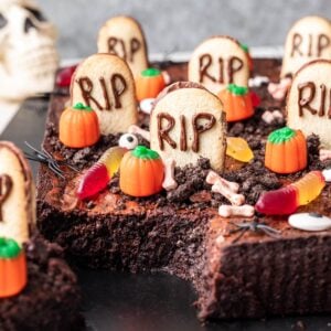 Graveyard brownies decorated with tombstone cookies, gummy worms, and candy pumpkins.