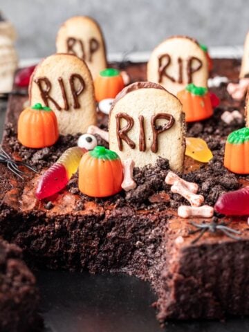 Graveyard brownies decorated with tombstone cookies, gummy worms, and candy pumpkins.
