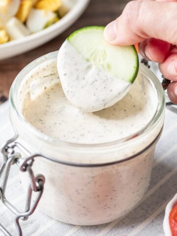 Dipping a cucumber in greek yogurt ranch dressing.