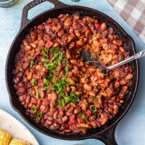 Smoked baked beans in a cast iron skillet with a serving spoon.