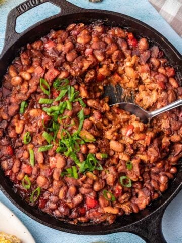 Smoked baked beans in a cast iron skillet with a serving spoon.