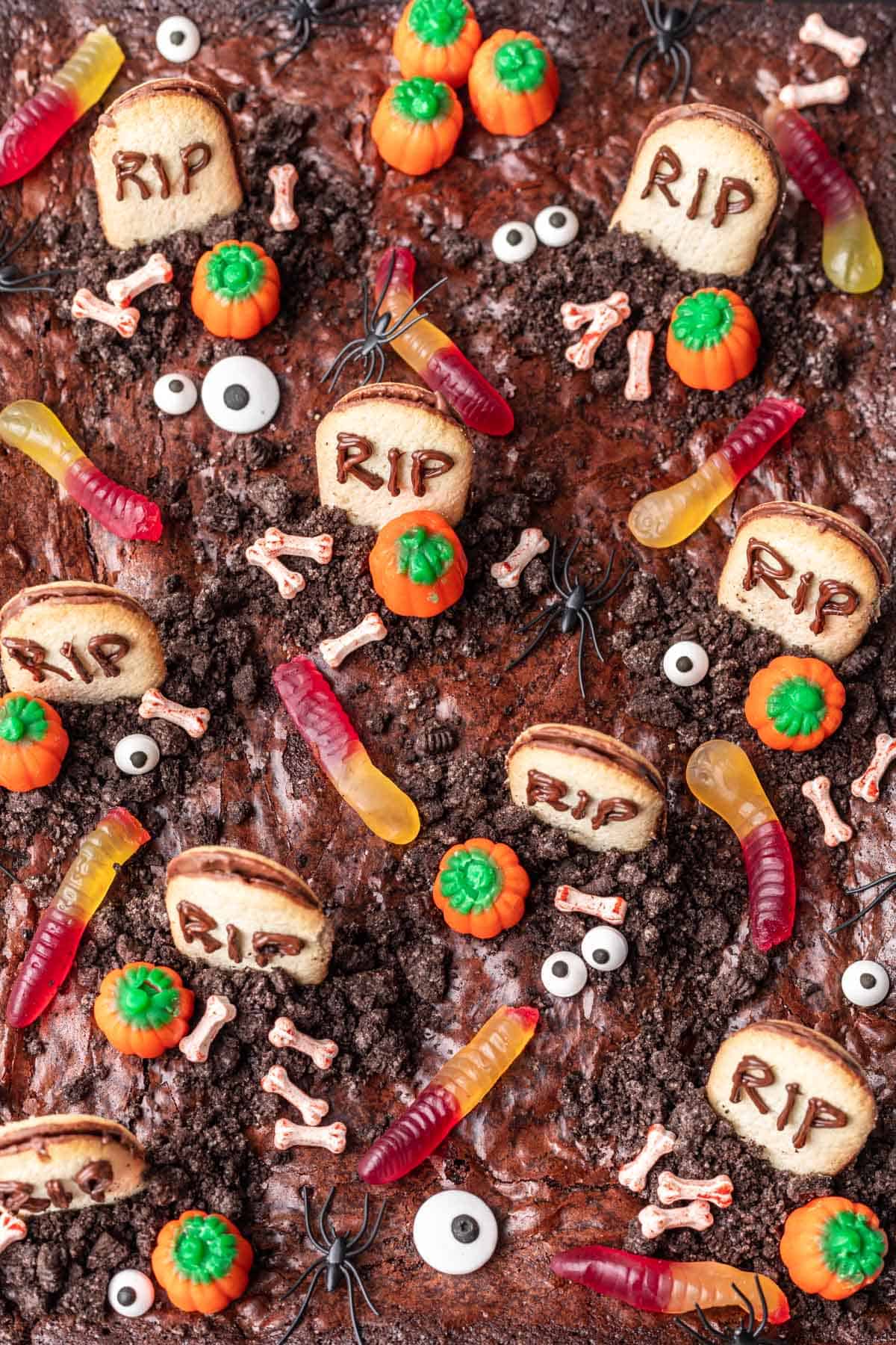 Birds eye view of graveyard brownies with tombstone cookies, candy bones, gummy worms, and oreo dirt.