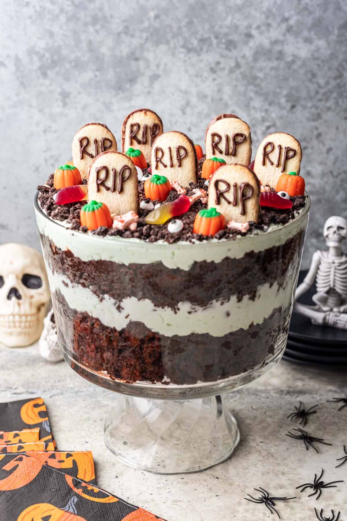Halloween trifle with edible decorations on top and layers of brownies and pistachio cream in the middle.