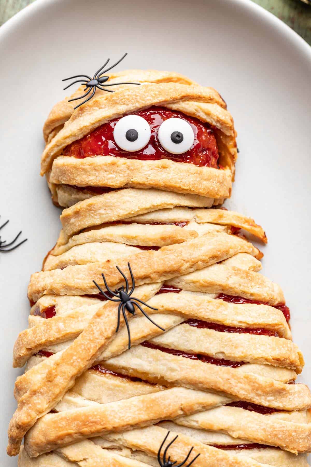 Close up of mummy meatloaf on a serving platter with fake spiders around it.