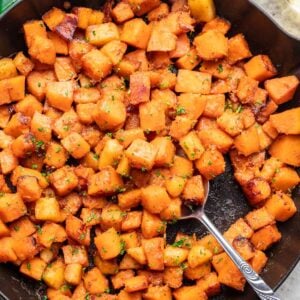 Sautéed butternut squash in a skillet with a spoon.
