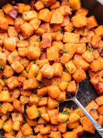 Sautéed butternut squash in a skillet with a spoon.