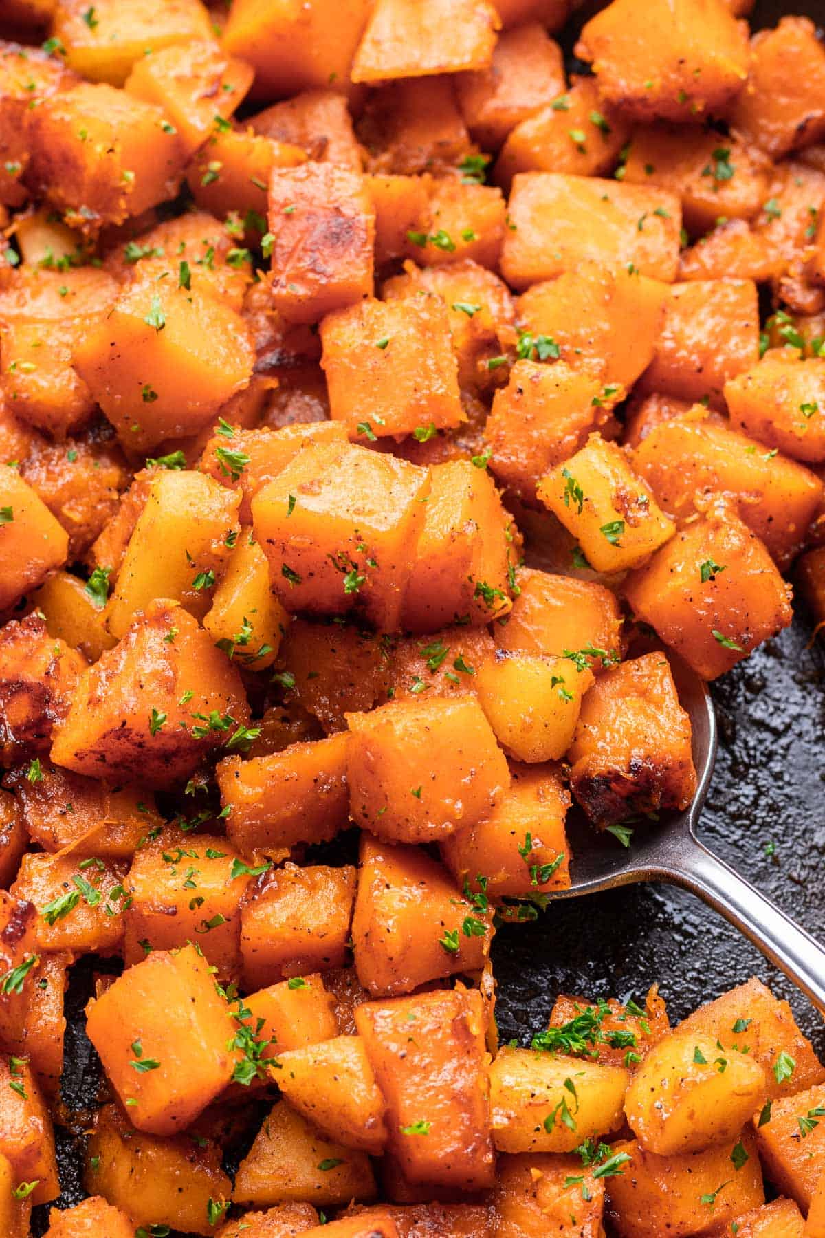 A serving spoon scooping sautéed butternut squash out of a skillet.