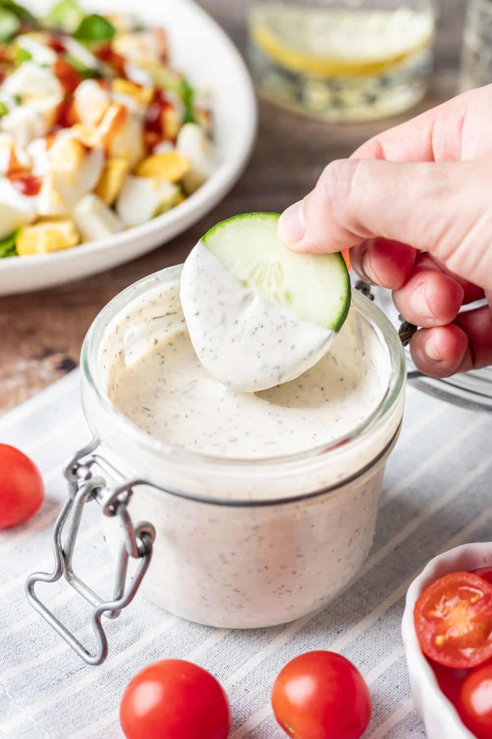 Greek yogurt ranch dressing in a jar with a cucumber dipped into it.