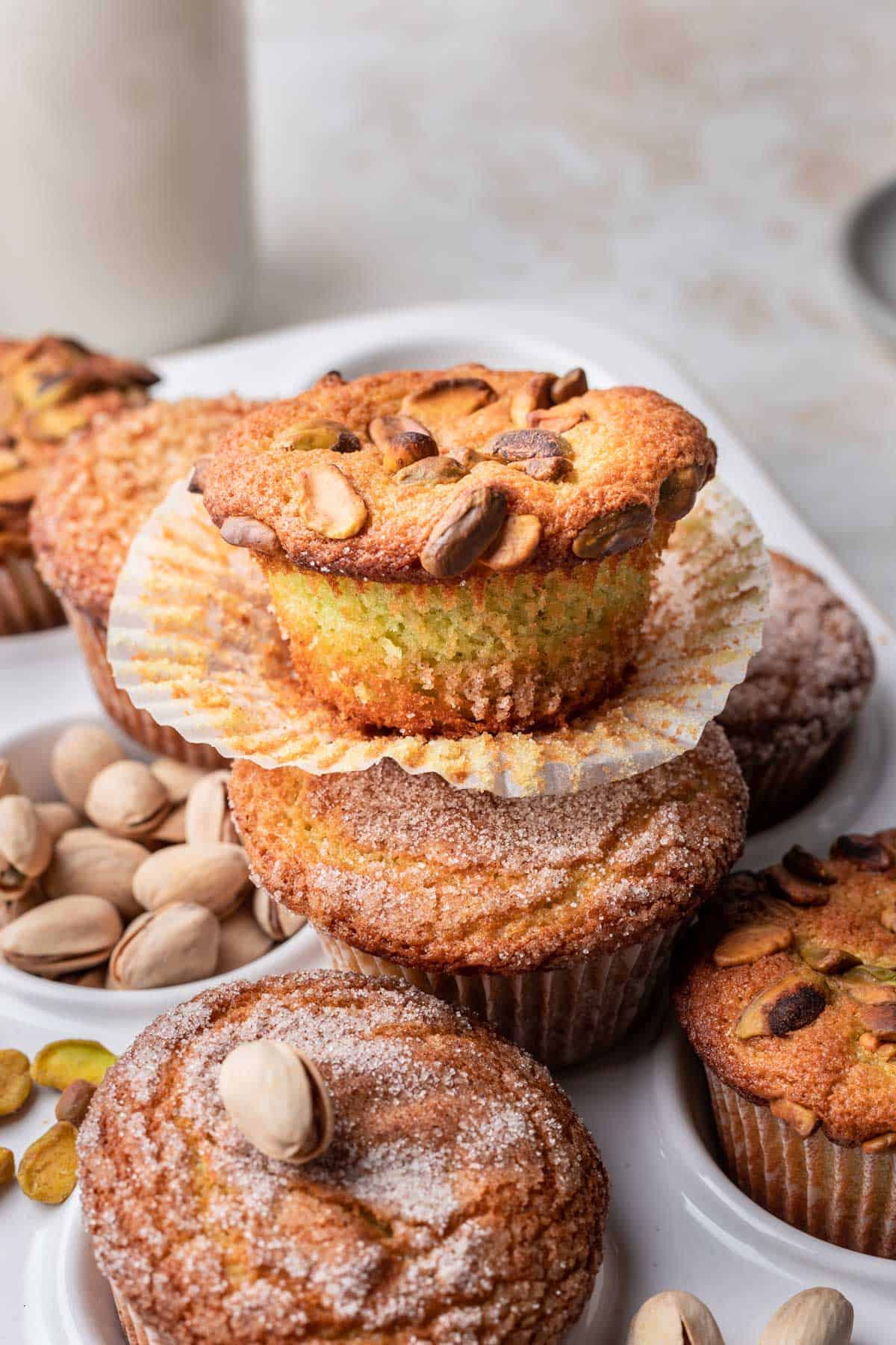 A pistachio muffin unwrapped on a tray of muffins.