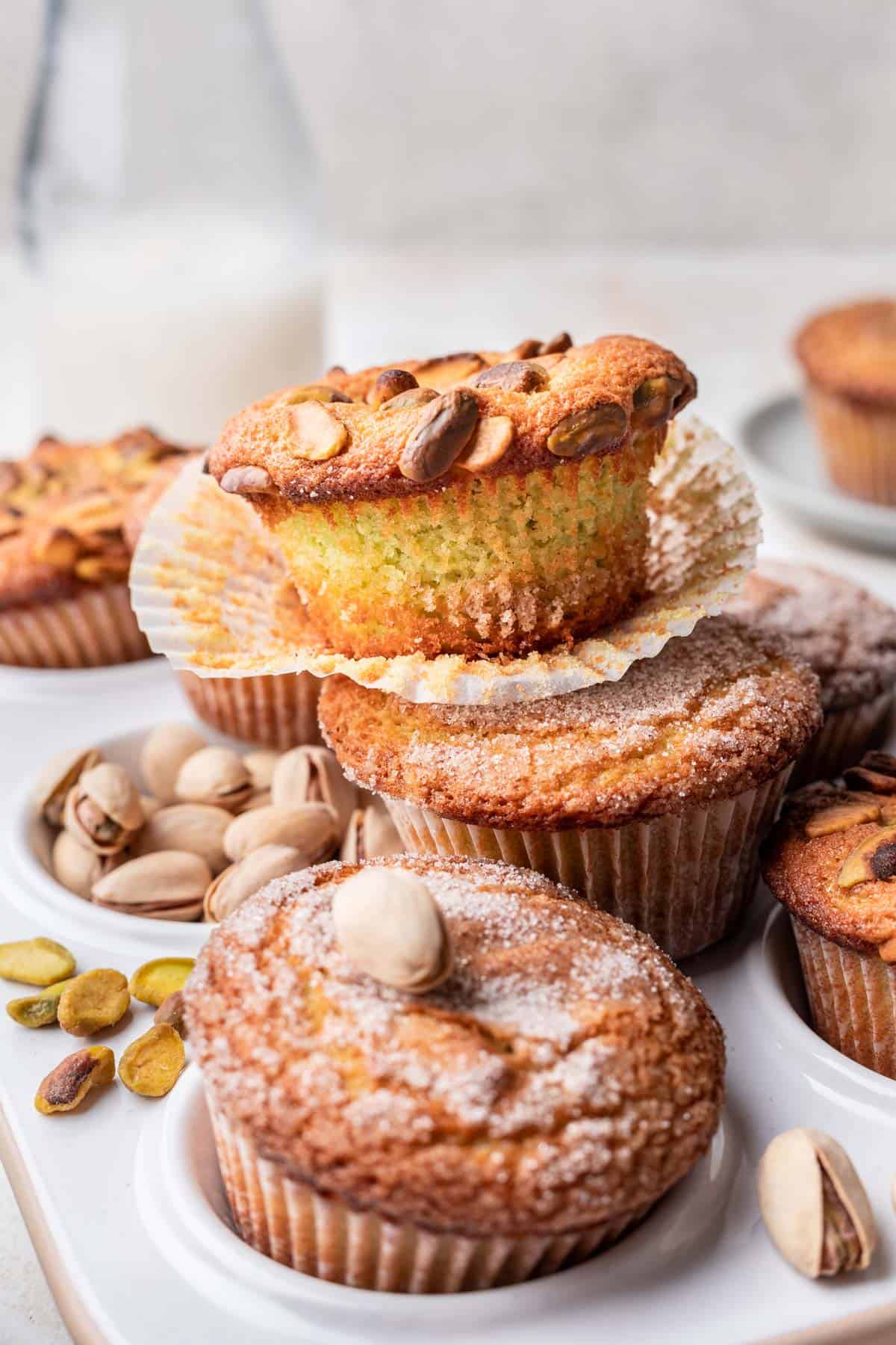 Pistachio muffins stacked on one another with pistachios around them.