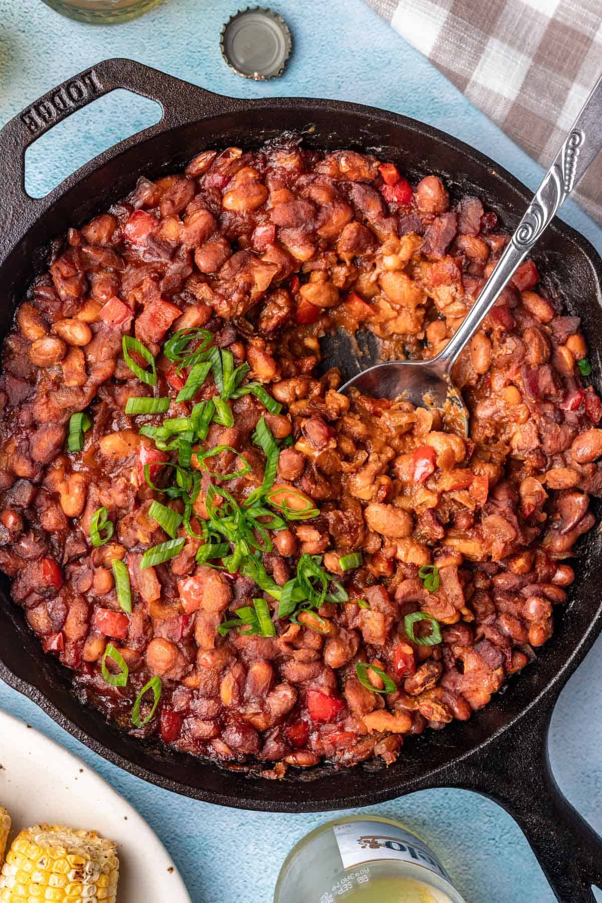 Smoked baked beans garnished with green onions in a cast iron skillet.